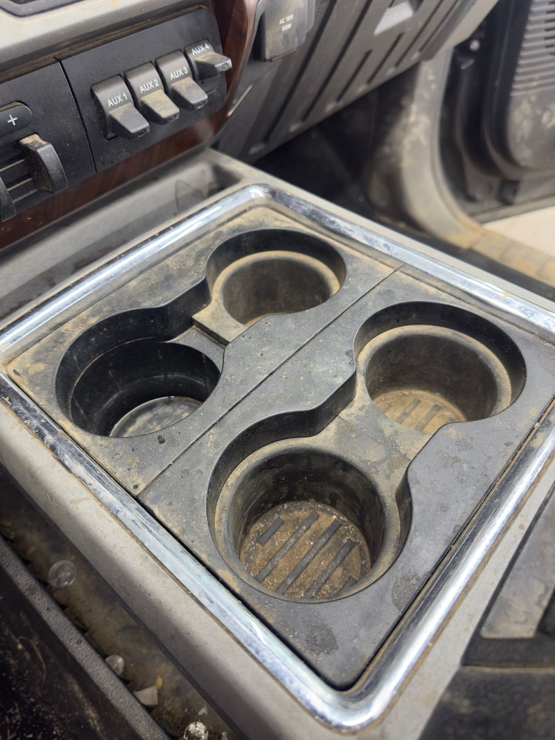 A dirty, black plastic vehicle center console with four built-in cupholders and a metallic frame.