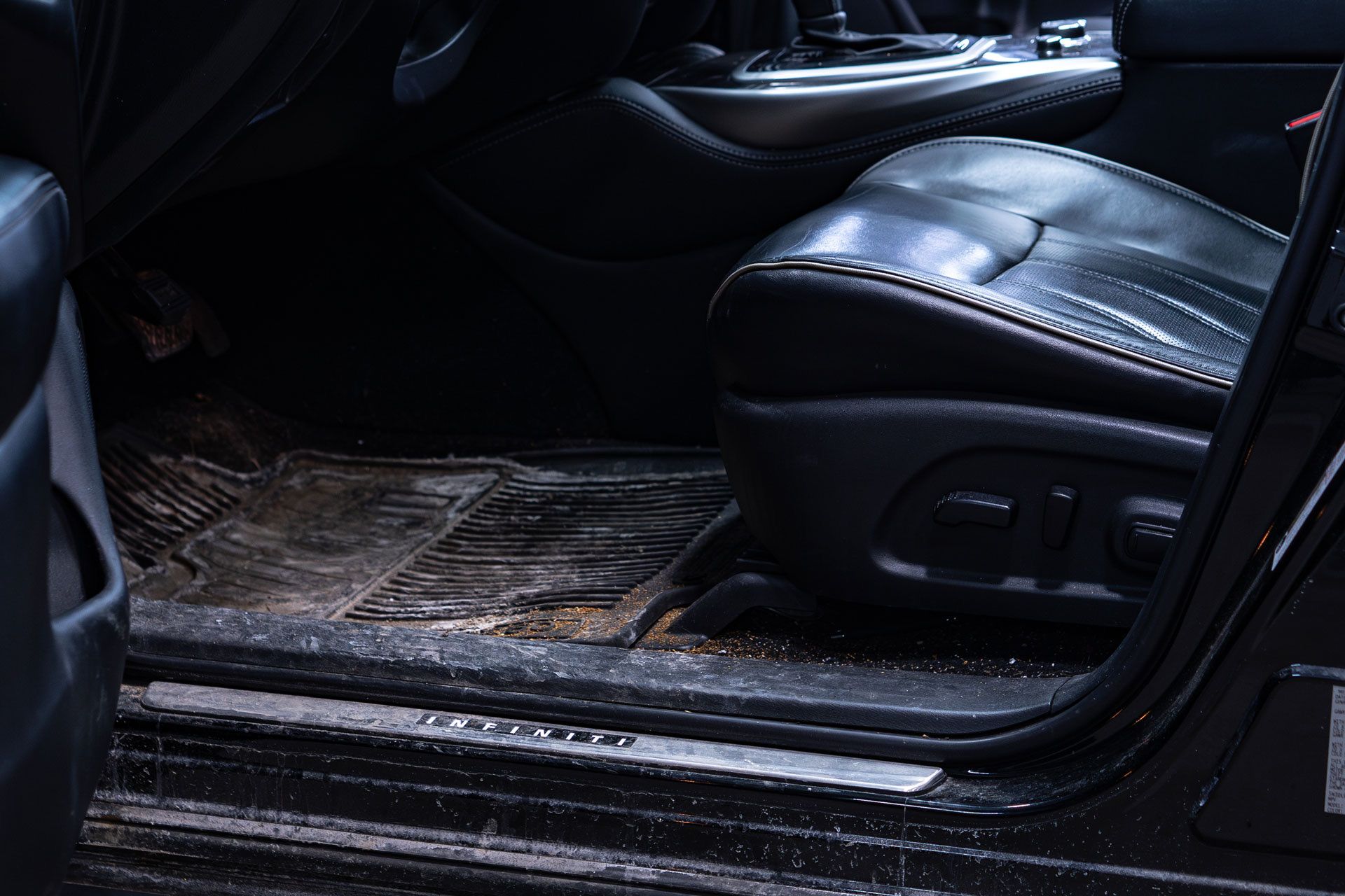 Close-up of a dirty car floor mat and a black leather driver's seat inside a vehicle.