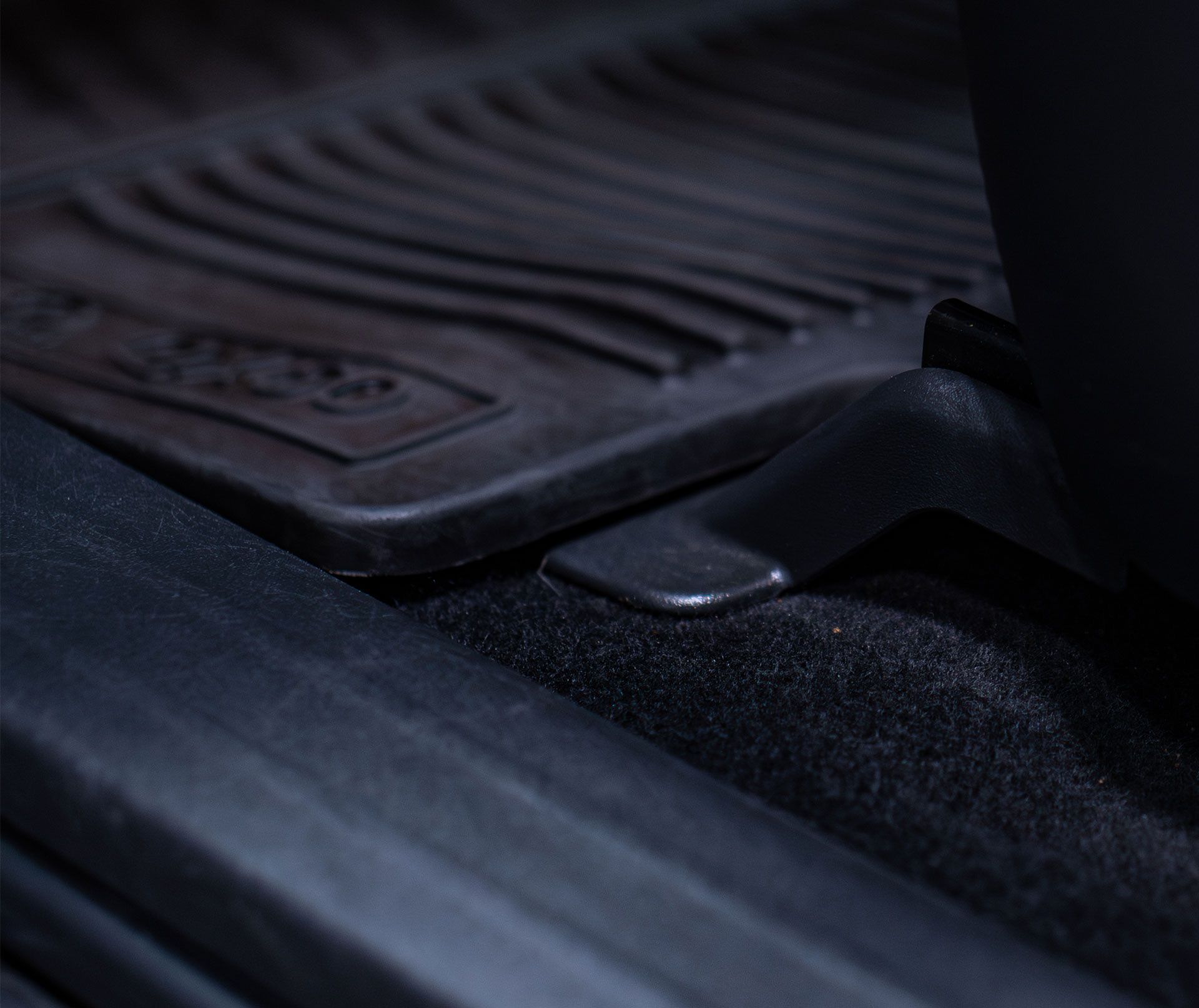 Close-up of a textured black rubber car floor mat installed near a vehicle seat rail and carpet.