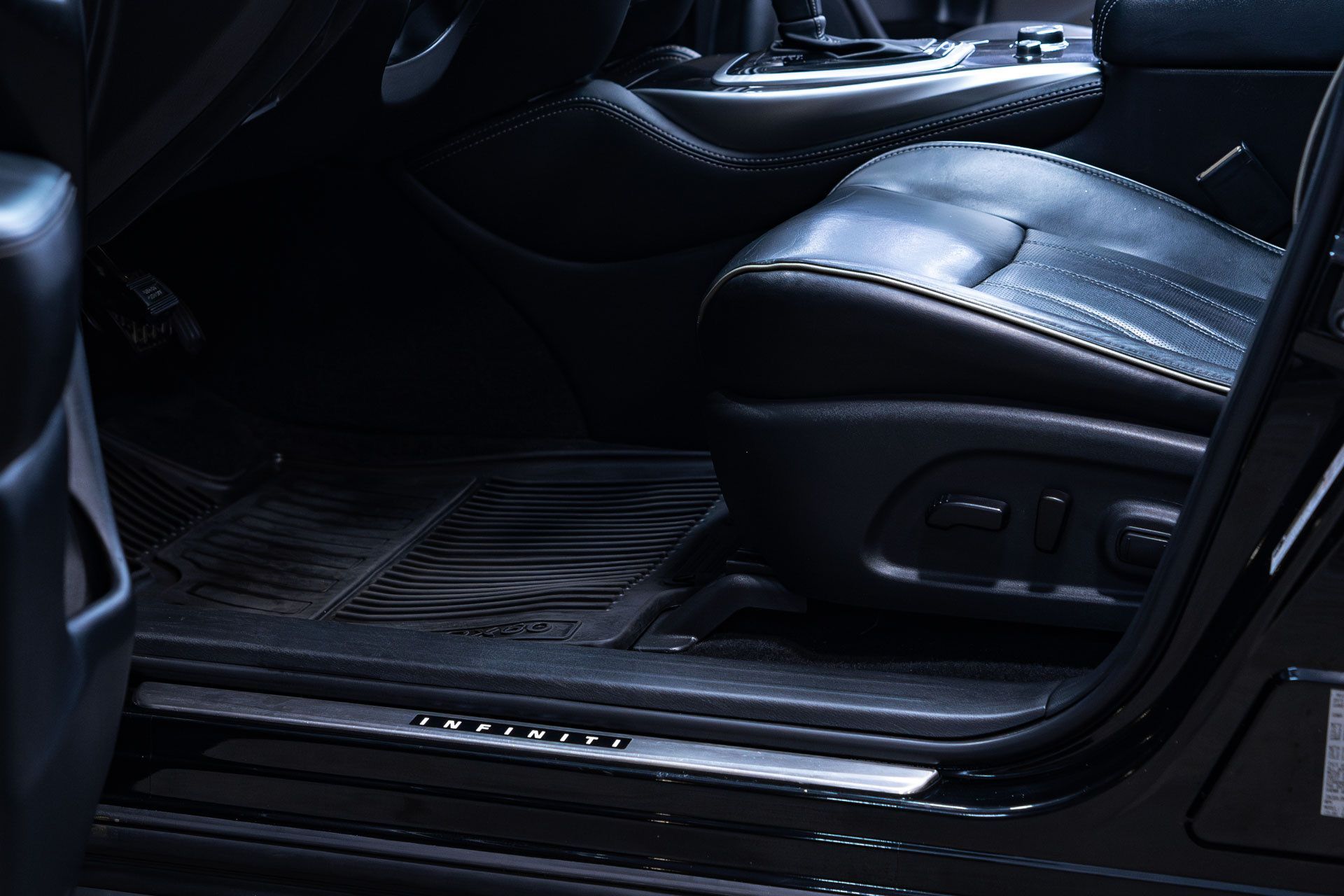A view of a car's black leather interior, focusing on the seat, footwell, and illuminated door sill plate.
