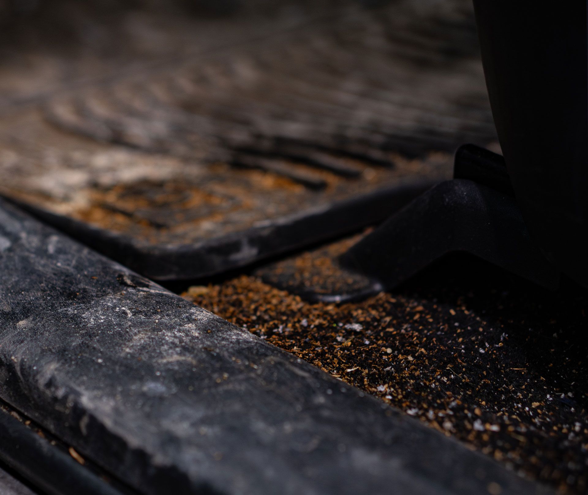 A close-up view of a car interior floor mat covered in brown dirt and debris near the vehicle's foot pedal.