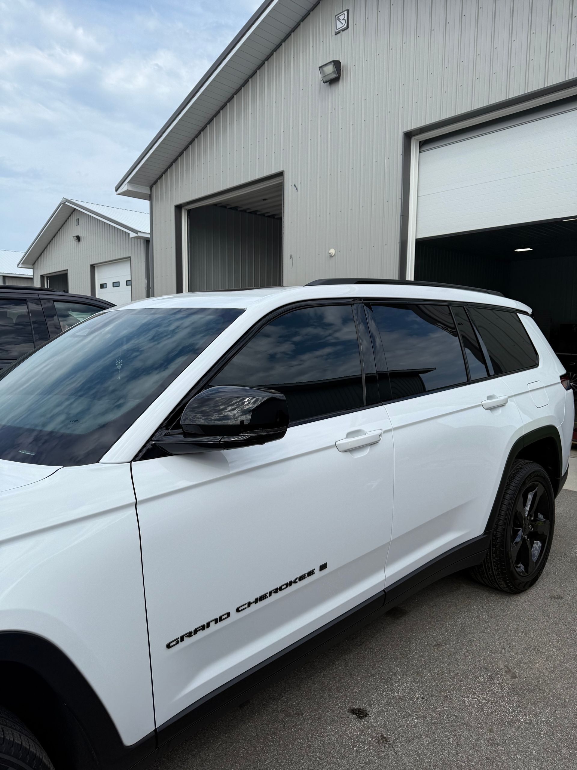 A white Grand Cherokee SUV parked outside a metal garage building.