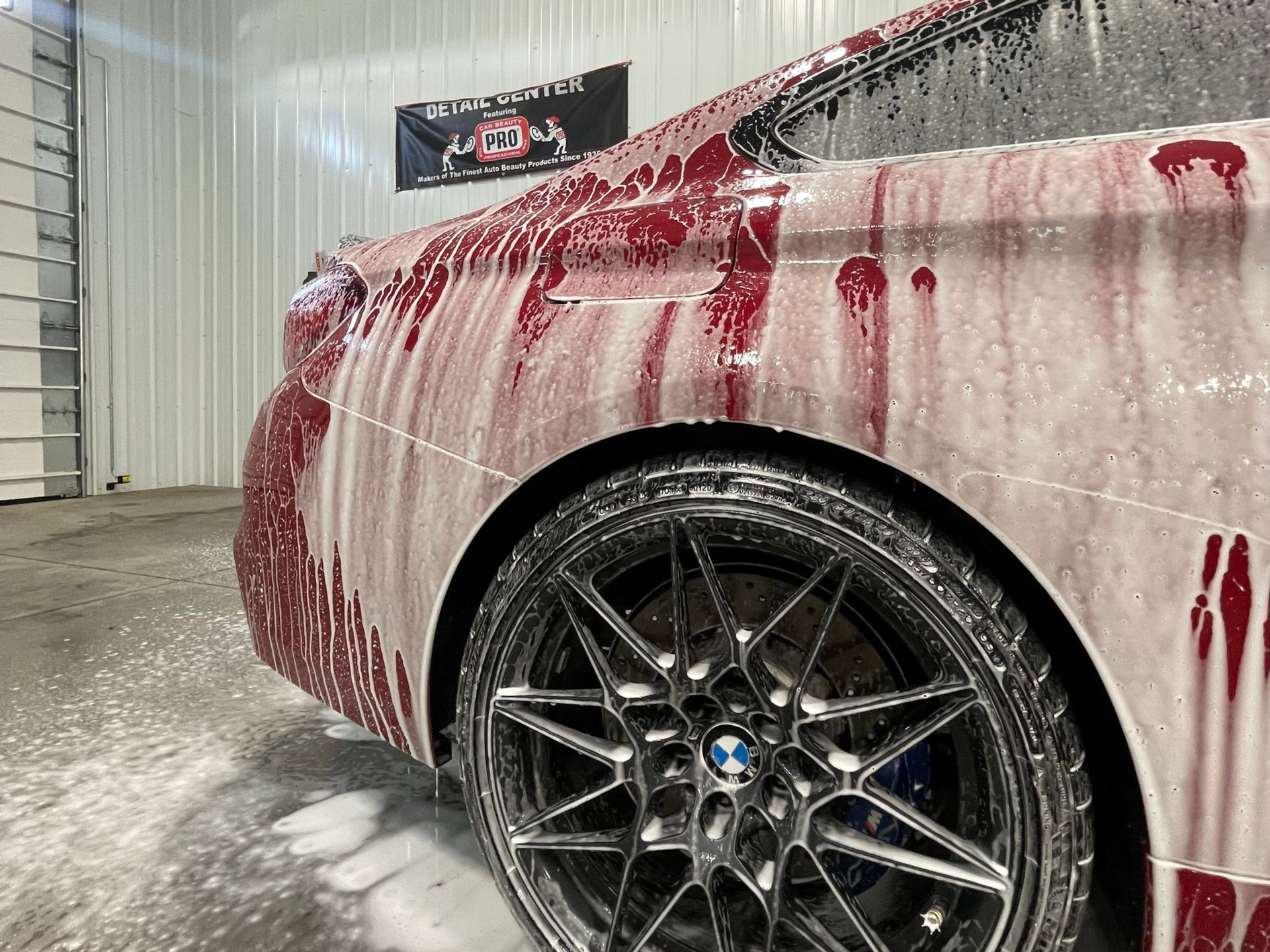 A bright red vintage car covered in white soap suds during a car wash.