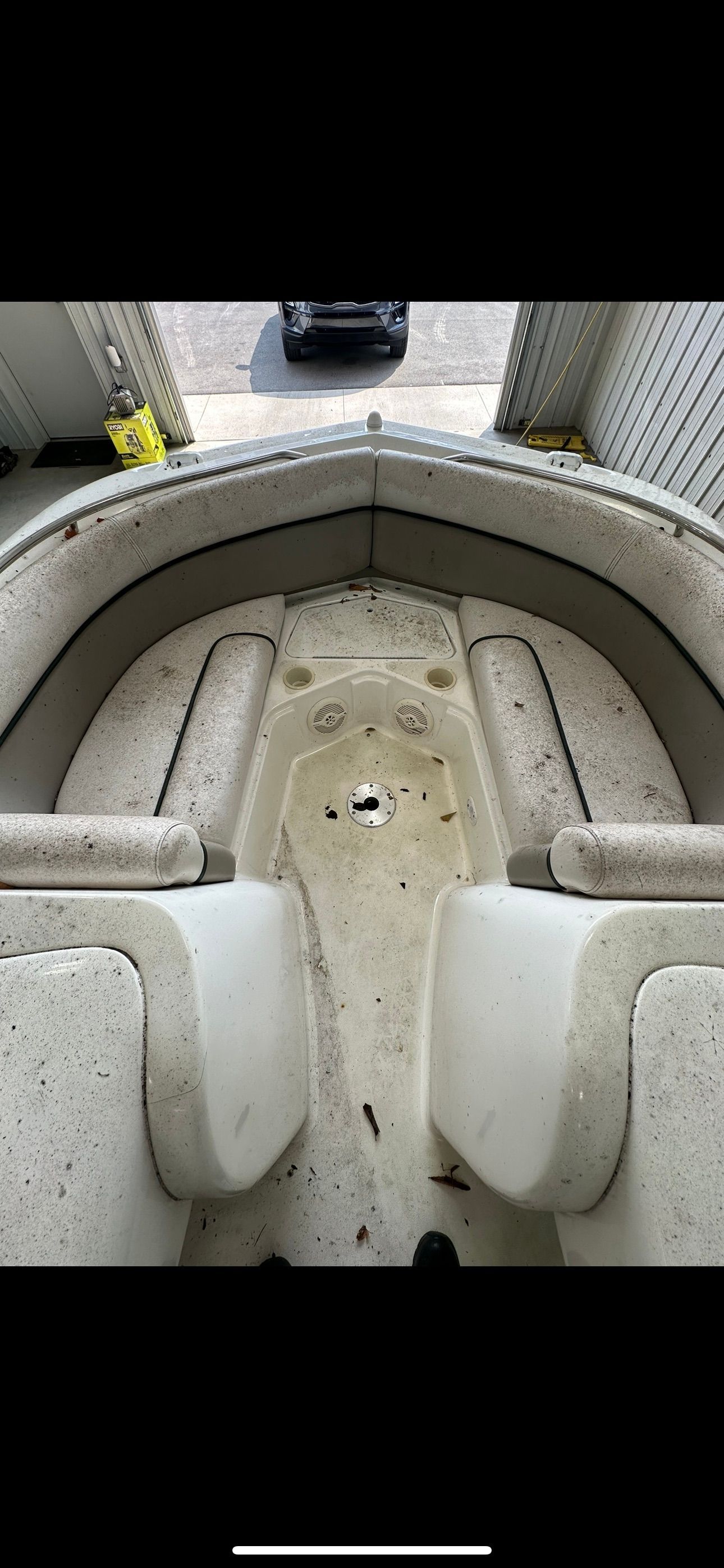 Interior view of a boat's front seating area with beige cushions and a floor littered with small dark debris.