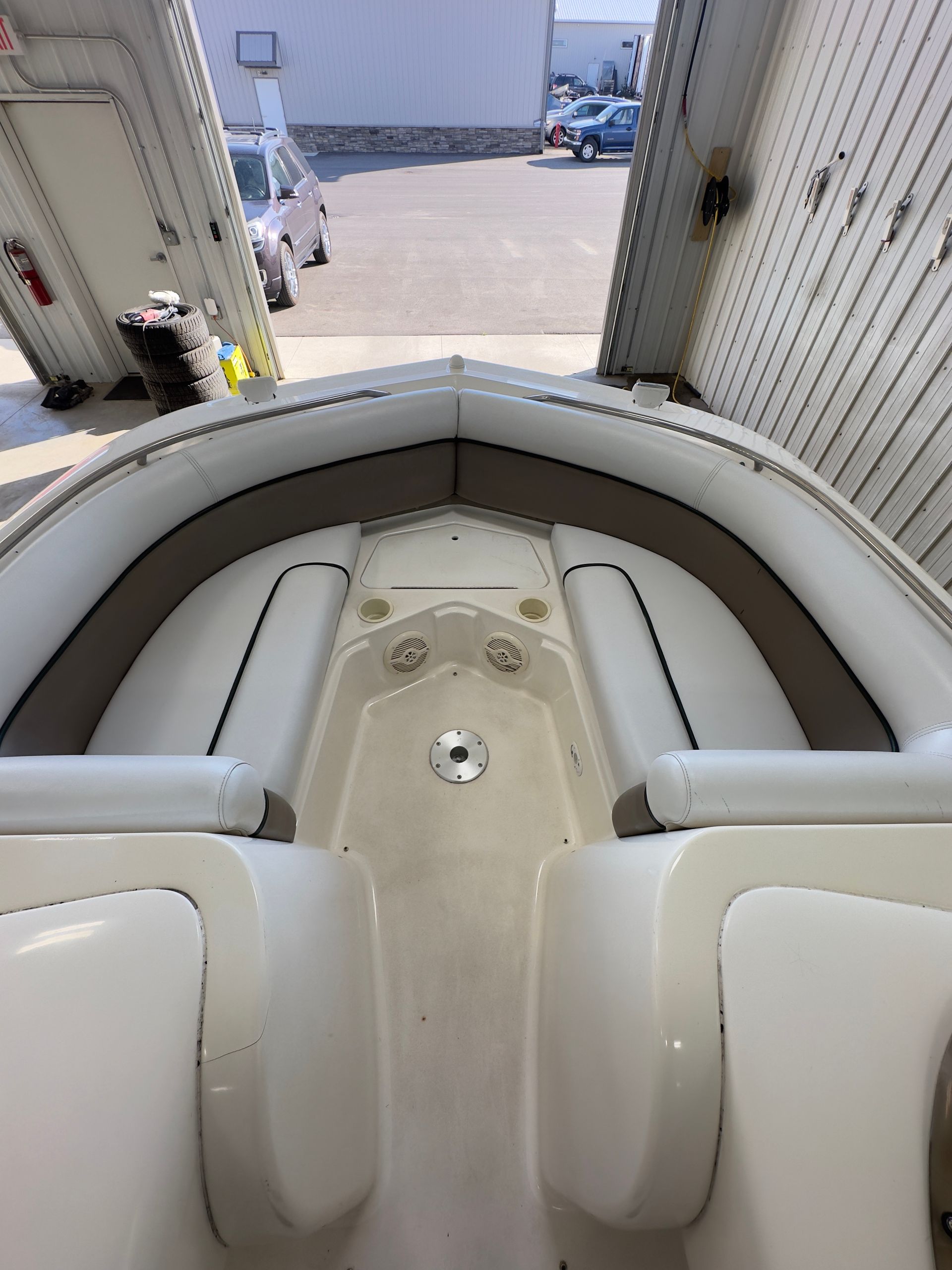 The interior bow seating area of a white boat, featuring neutral cushions and a central table pedestal in a workshop.