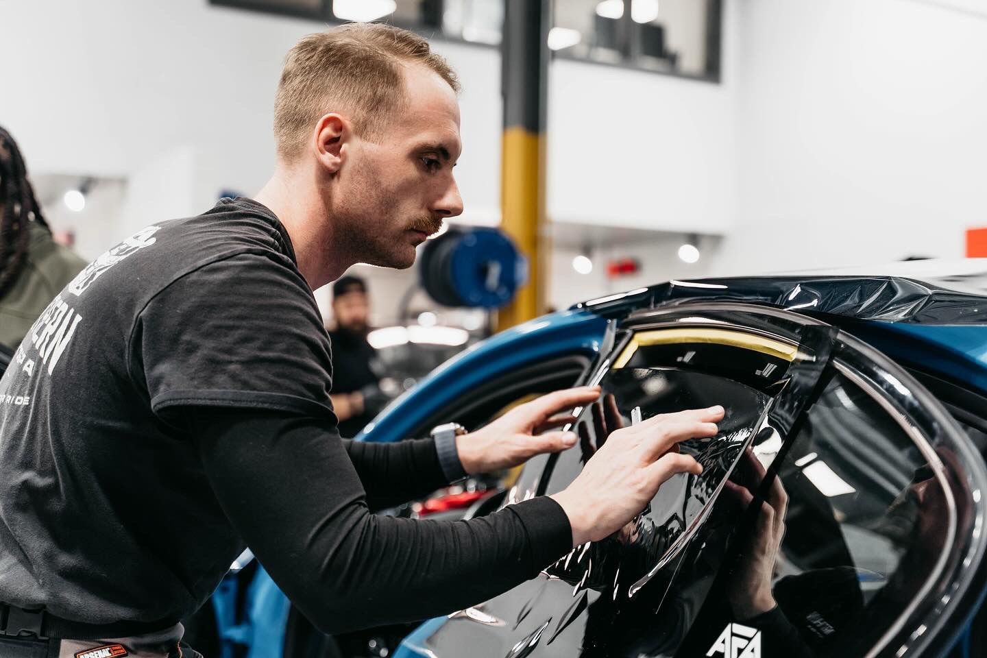 A technician carefully applies window tint film to a car door in a well-lit workshop.