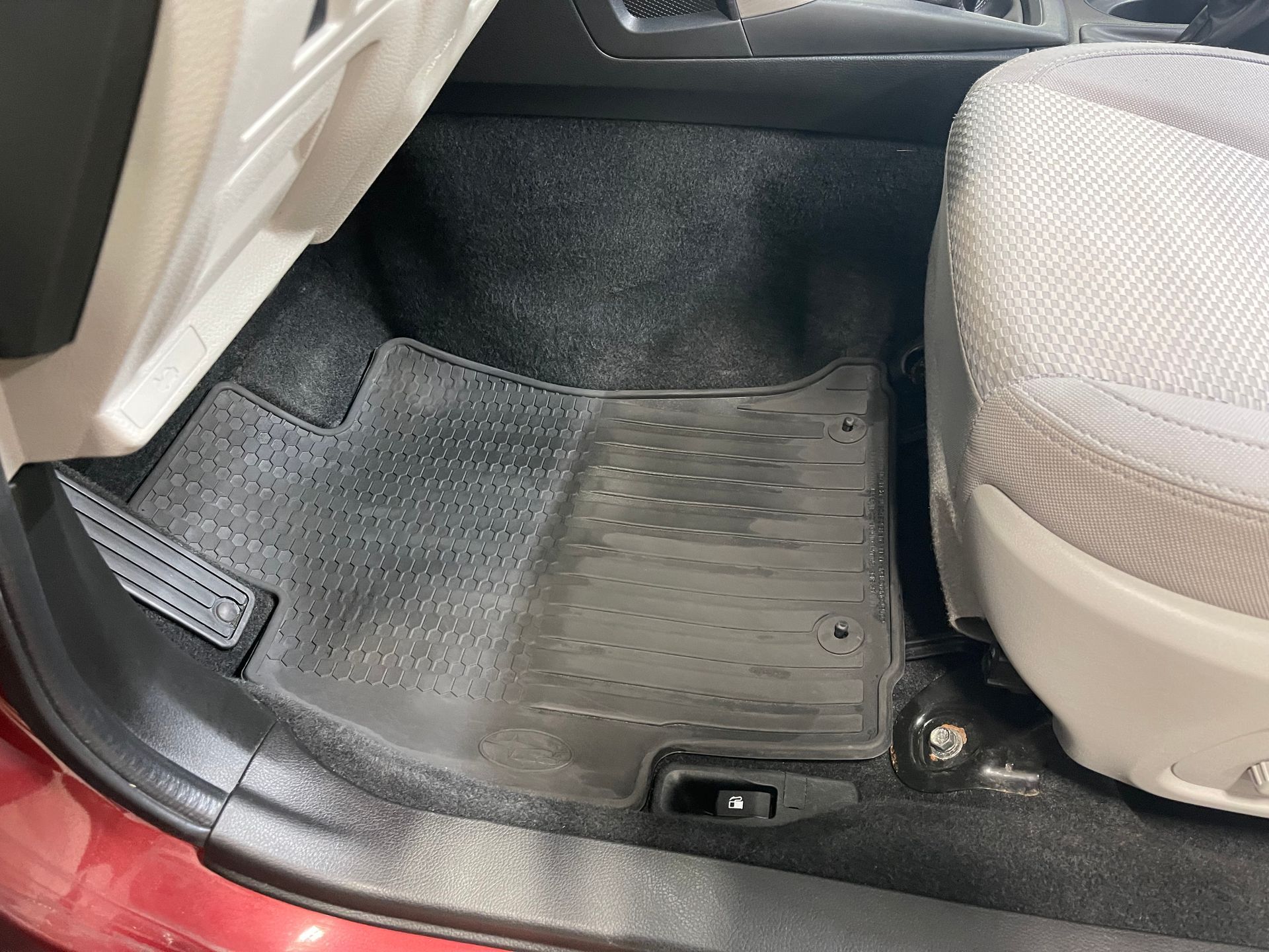The front passenger side interior of a vehicle, showing a black rubber floor mat resting on dark grey carpeting.