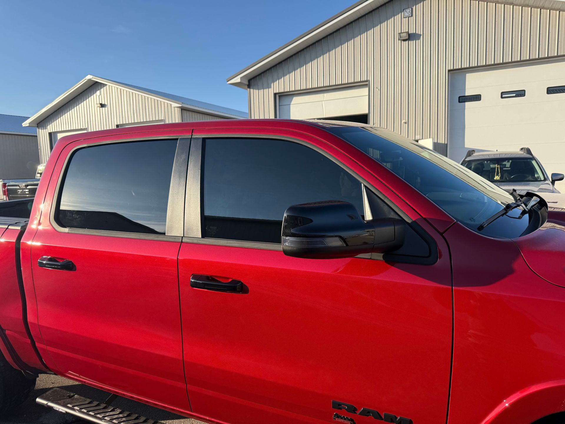 A bright red Ram pickup truck with tinted windows parked outside a large metal workshop on a sunny day.