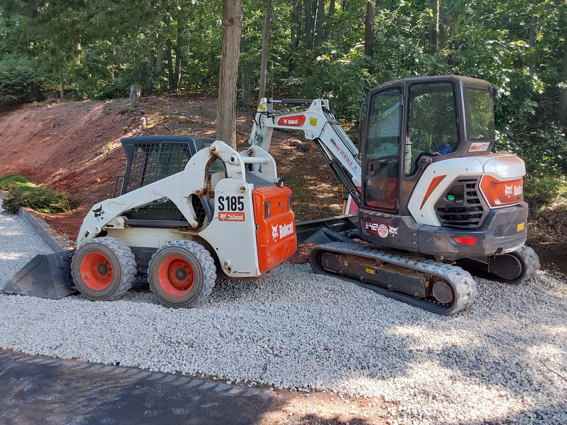 a bobcat skid steer and excavator are parked next to each other on gravel