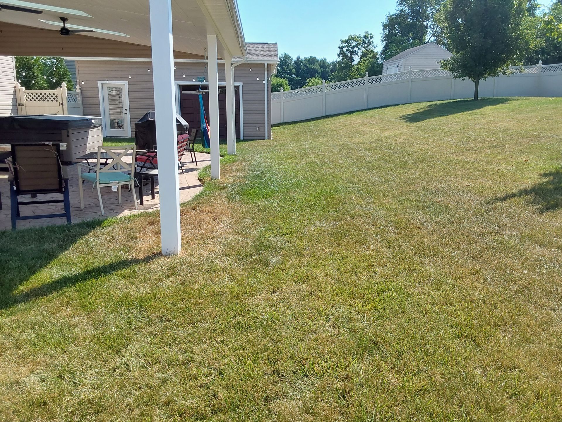 a lush green lawn with a white fence and a patio area in the background