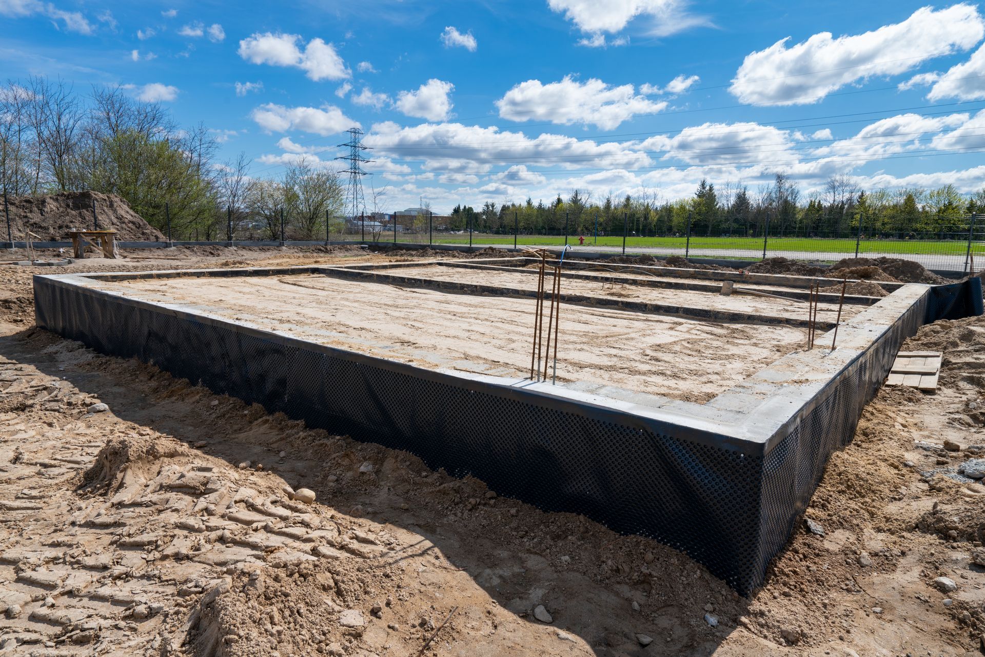 Foundation slab under construction on a dirt lot with wooden forms and a cloudy blue sky