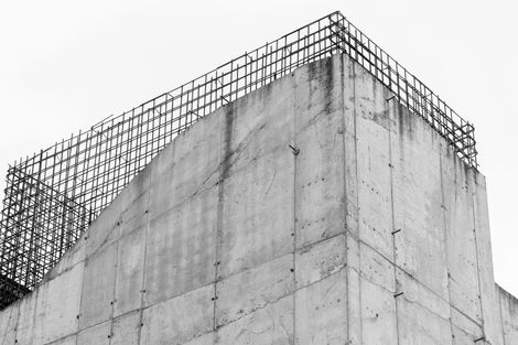 Concrete building corner with exposed rebar against a cloudy sky