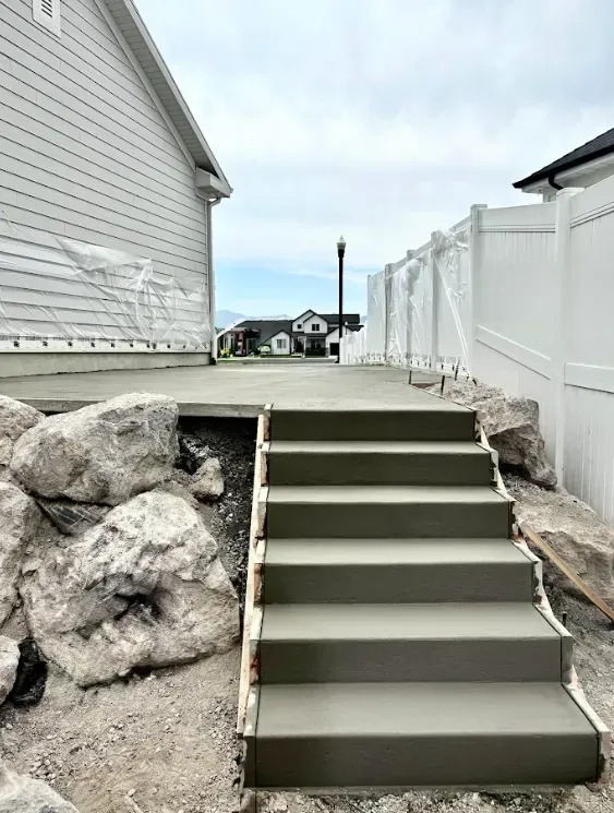 Concrete stairs between a house and white fence, bordered by large rocks