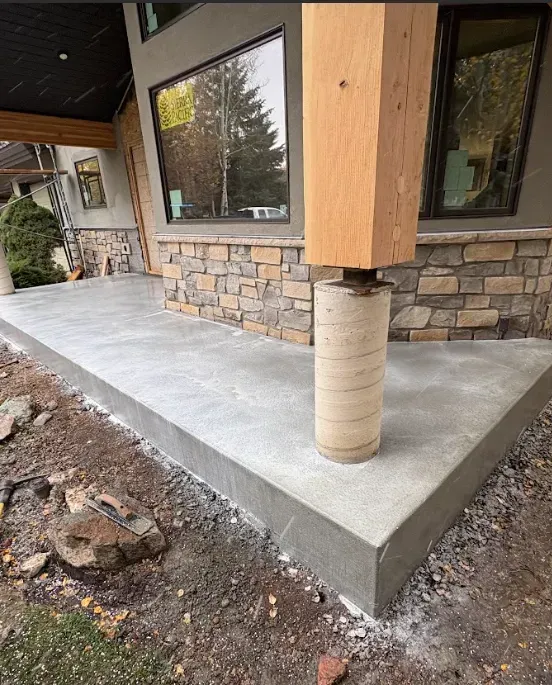 Concrete porch with a wooden post wrapped in protective material beside stone siding and large windows