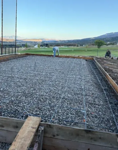 Concrete foundation under construction with rebar and workers in a field at sunset