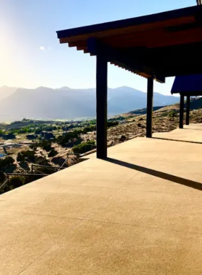 Desert mountain view from a shaded patio with sunlit stone floor and wooden roof posts