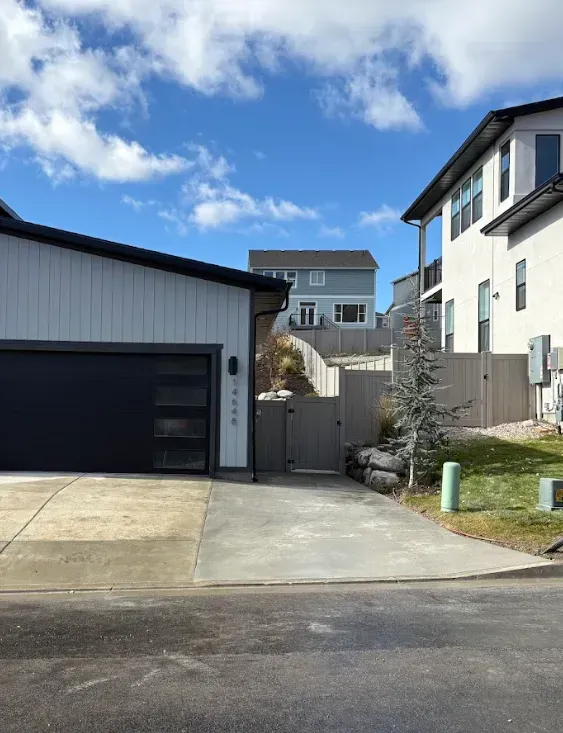 Suburban driveway between two houses, with a garage on the left and a gated walkway in the center.
