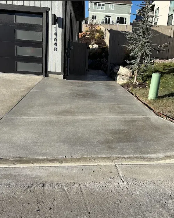 Concrete driveway leading to a gated side yard beside a modern garage and house, with lawn and utility box.