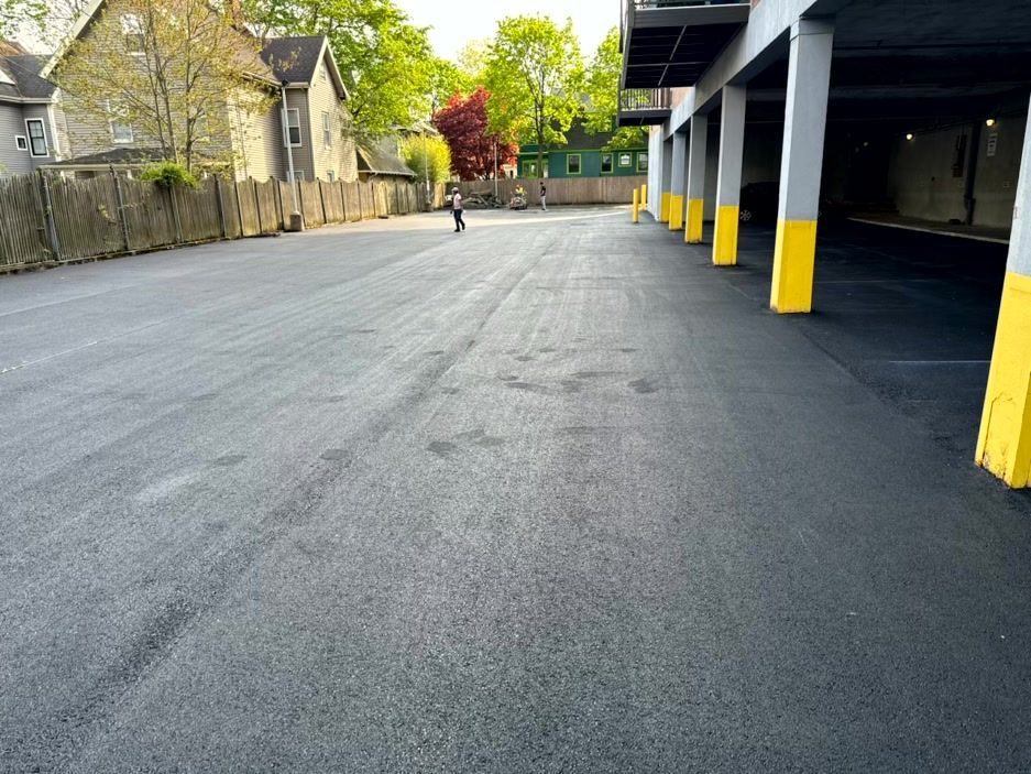 Newly paved asphalt parking area with yellow-trimmed columns on the right and a person walking in the distance.
