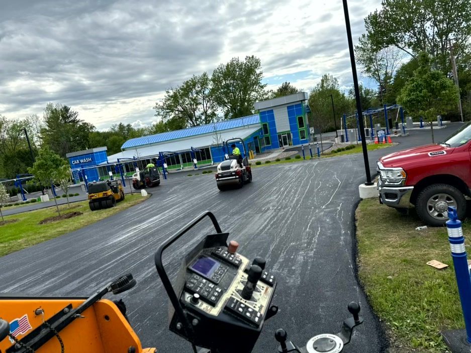 Asphalt paving at car wash entrance; blue and white building in background, red truck, dark sky.
