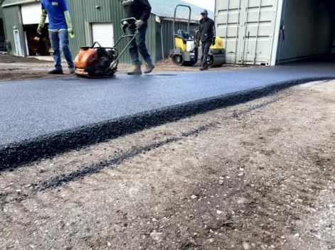 Workers paving asphalt surface with compacting equipment outdoors.