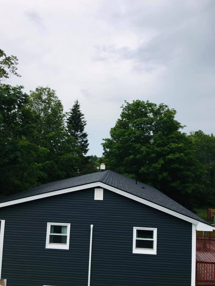 A blue house with a white trim and a roof surrounded by trees