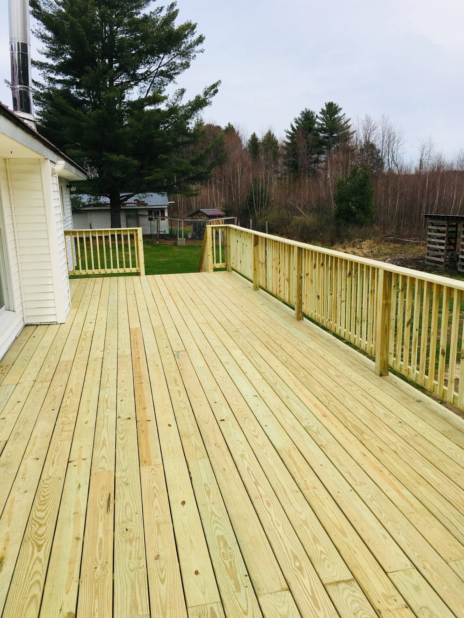 A large wooden deck with a railing and trees in the background