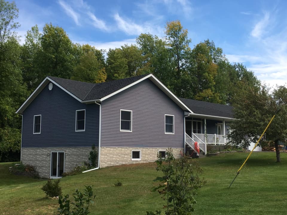 A gray house with a black roof is surrounded by trees