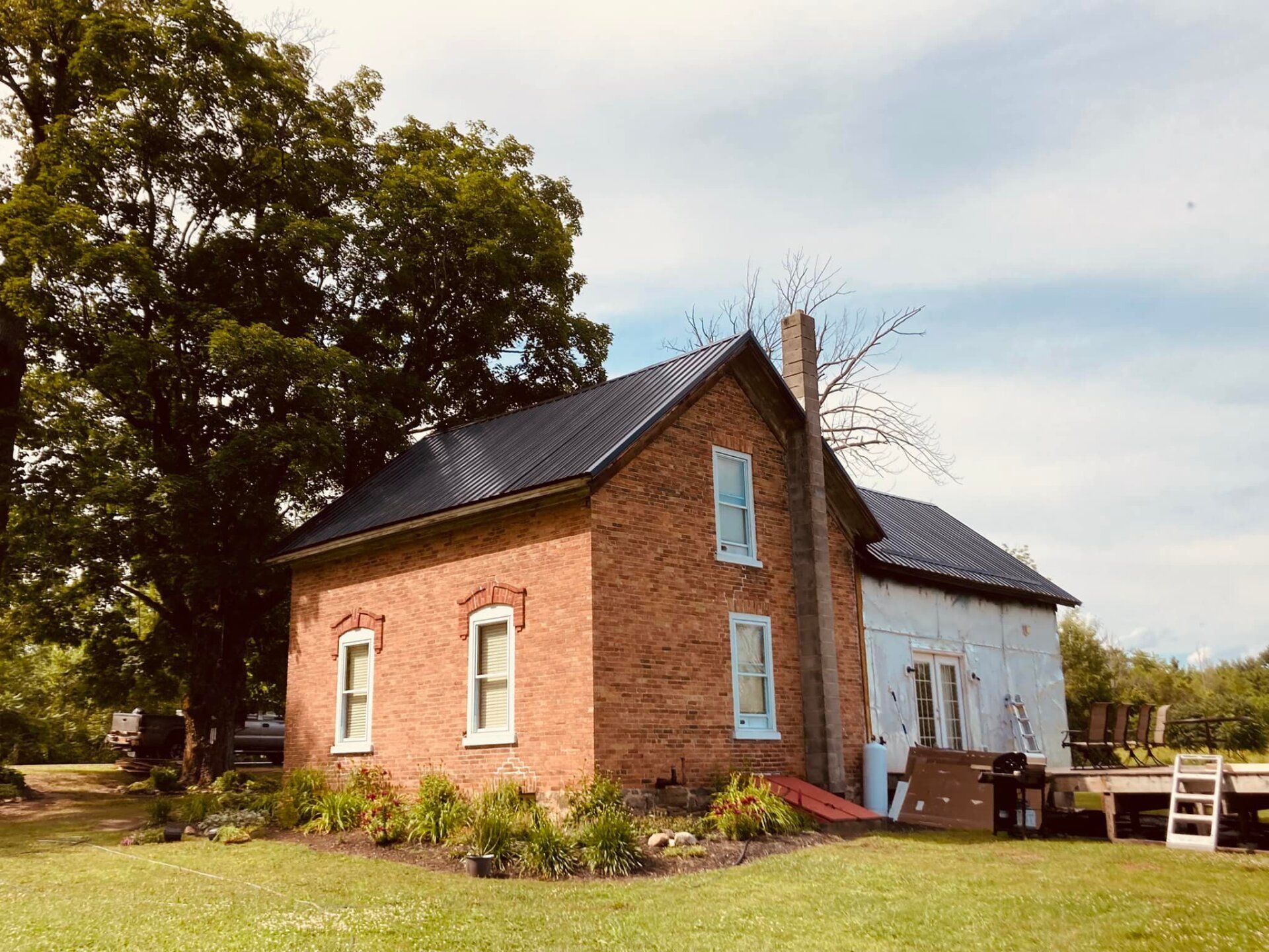 A brick house with a black roof is sitting in the middle of a grassy field.