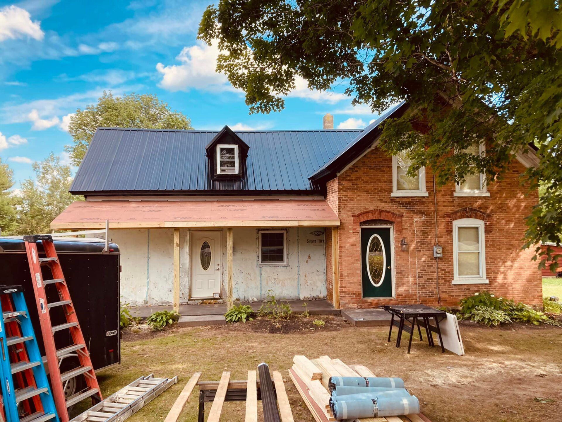 A brick house with a blue roof is being remodeled.