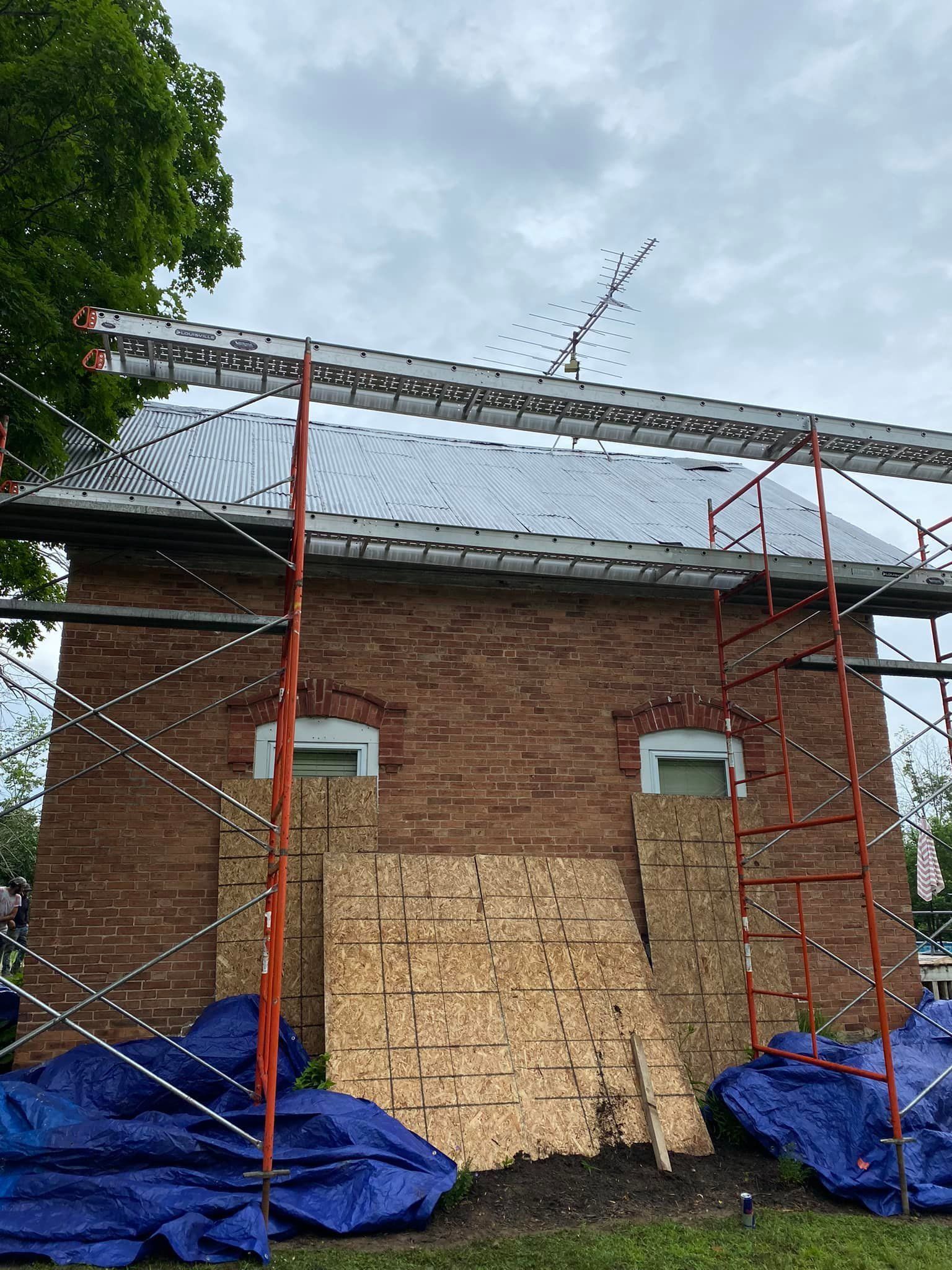A brick building is being remodeled with scaffolding and blue tarps.