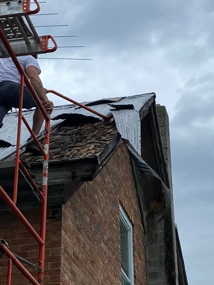 A man is sitting on a scaffolding on top of a brick building.