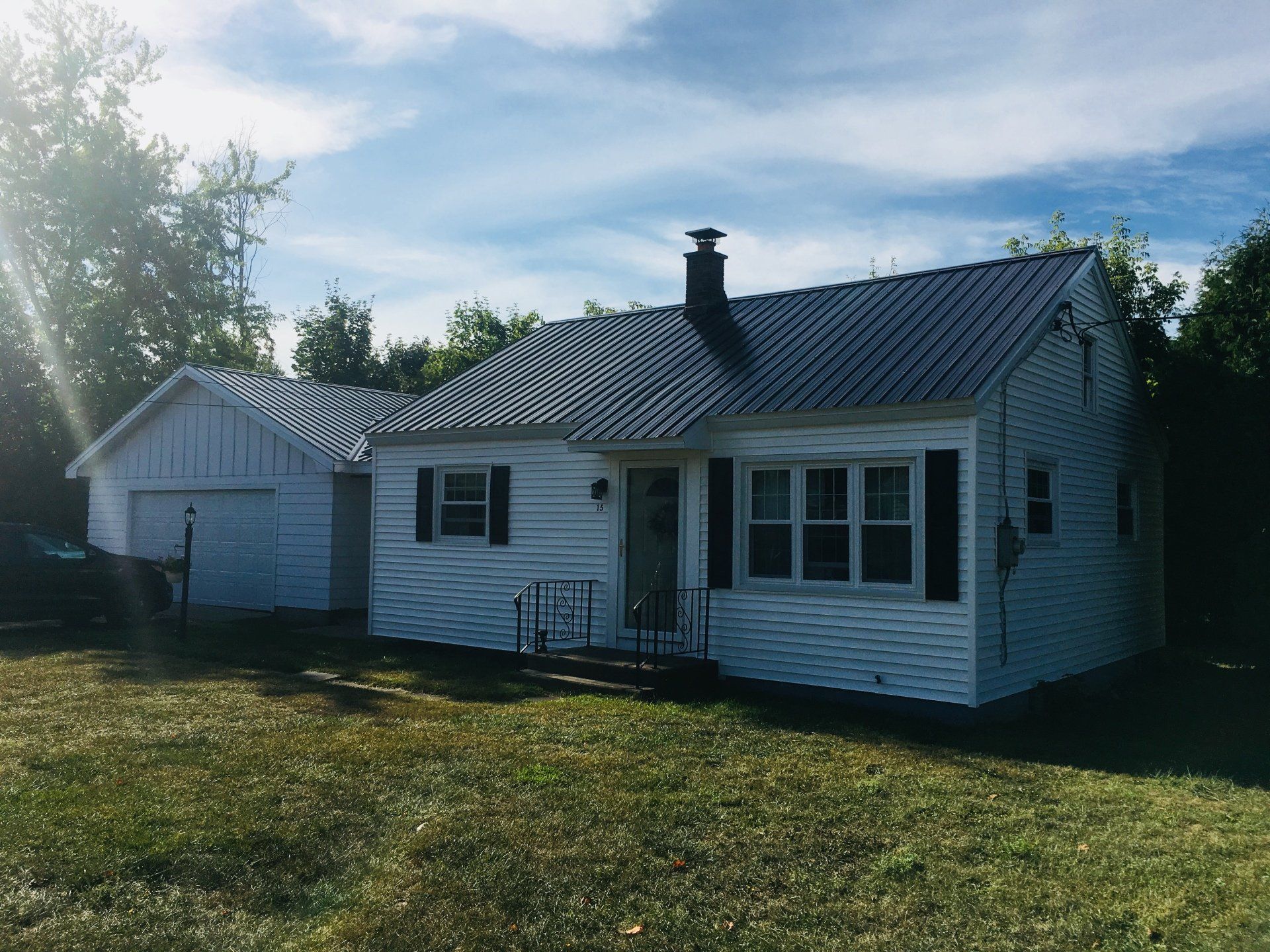 A white house with a metal roof is sitting in the middle of a grassy field.