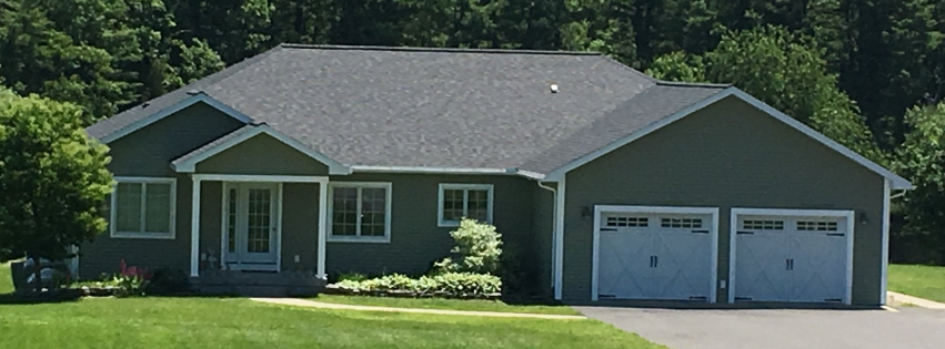 A large house with two garage doors is surrounded by trees