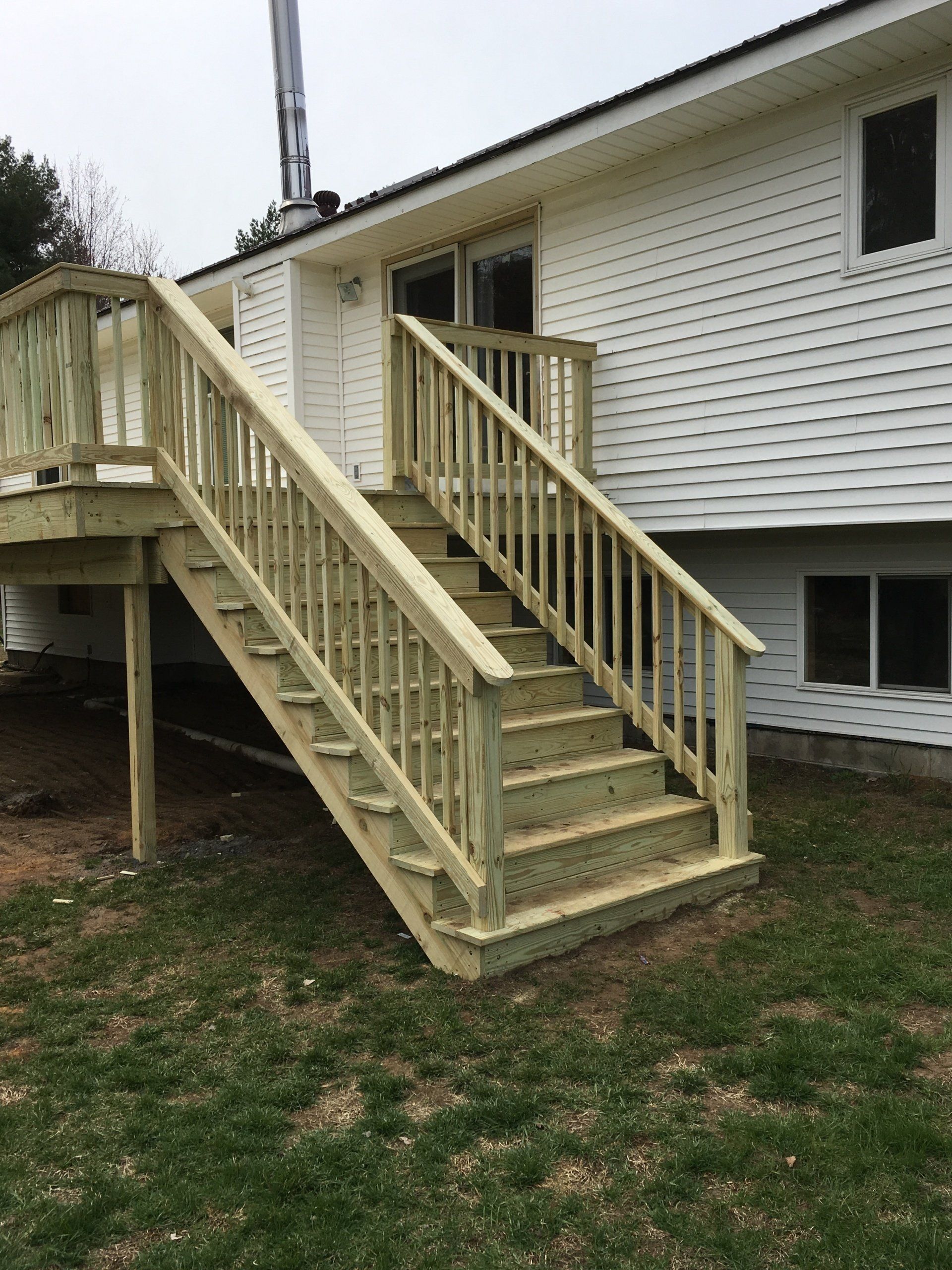 A wooden deck with stairs leading up to it is in front of a white house.