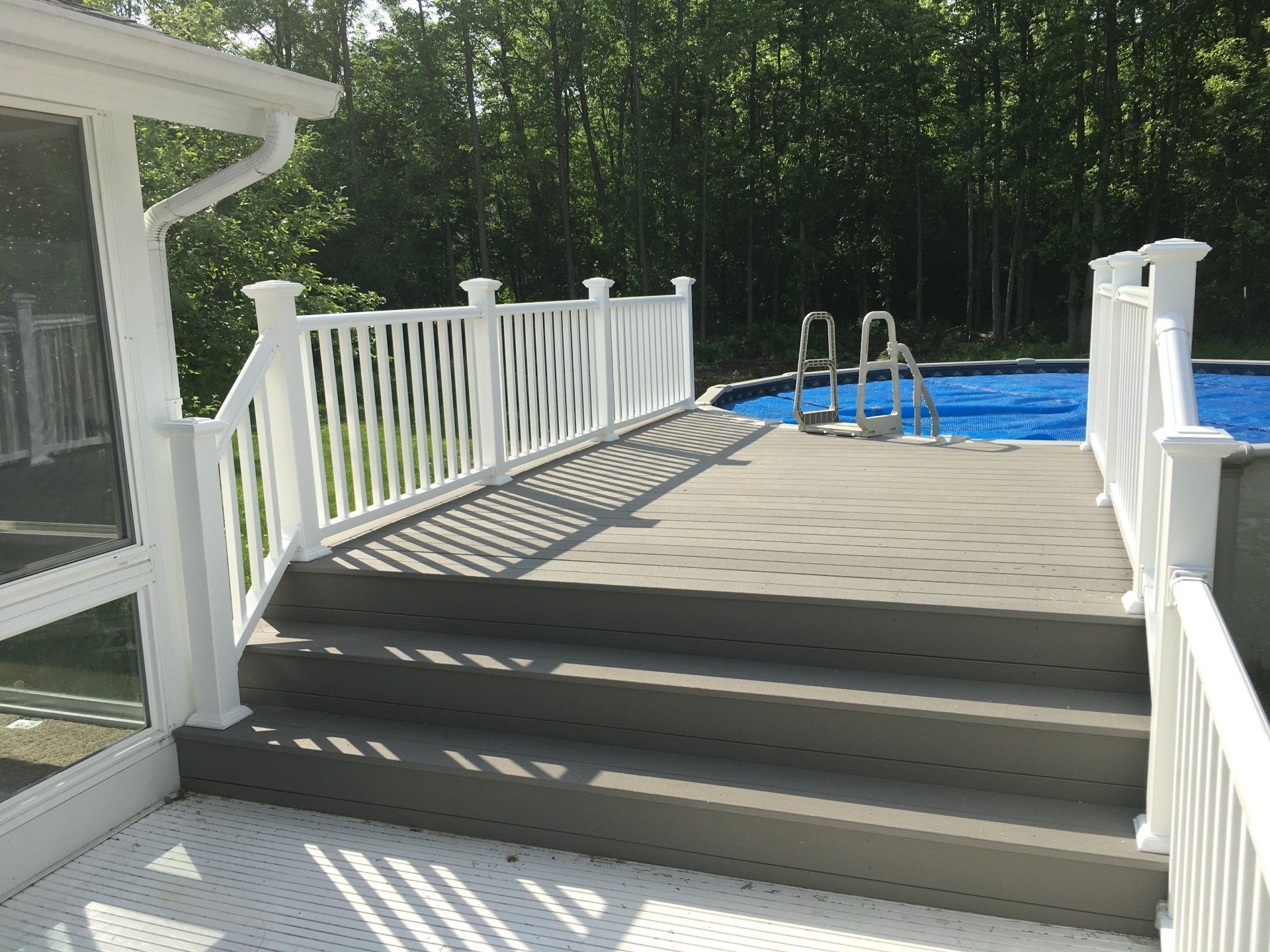 A white deck with stairs leading to a swimming pool.