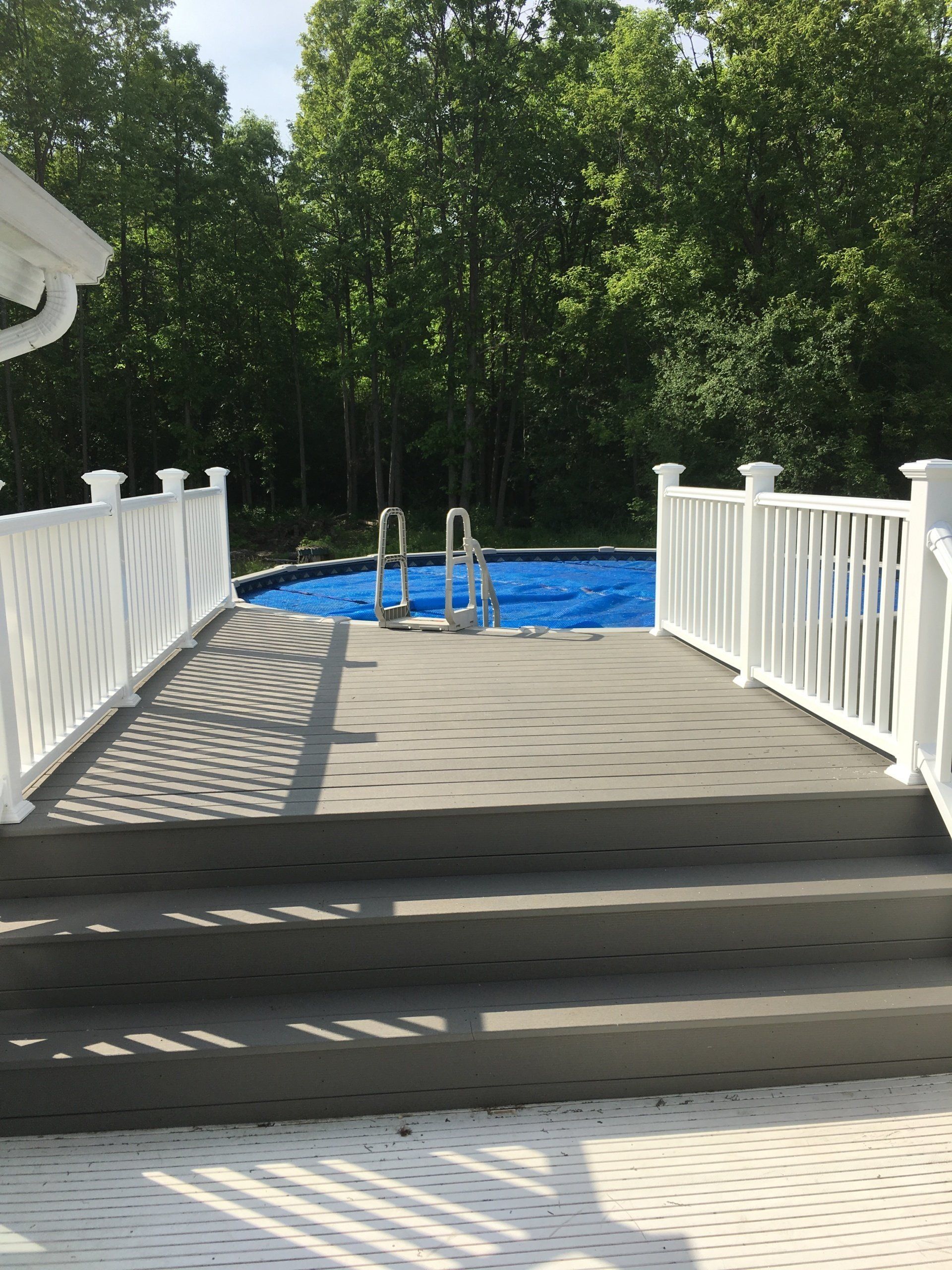 A deck with stairs leading to a swimming pool surrounded by trees.