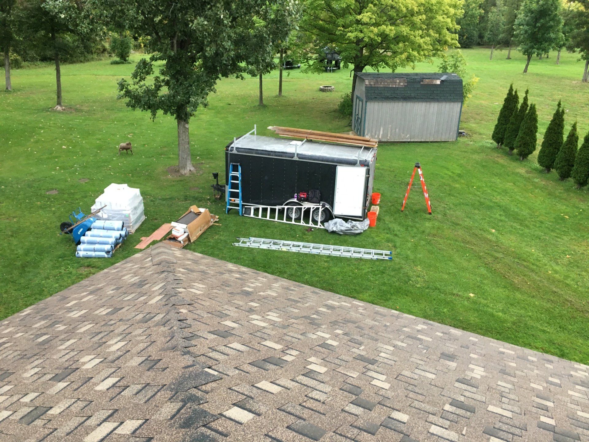 A trailer is sitting on top of a brick driveway next to a shed.