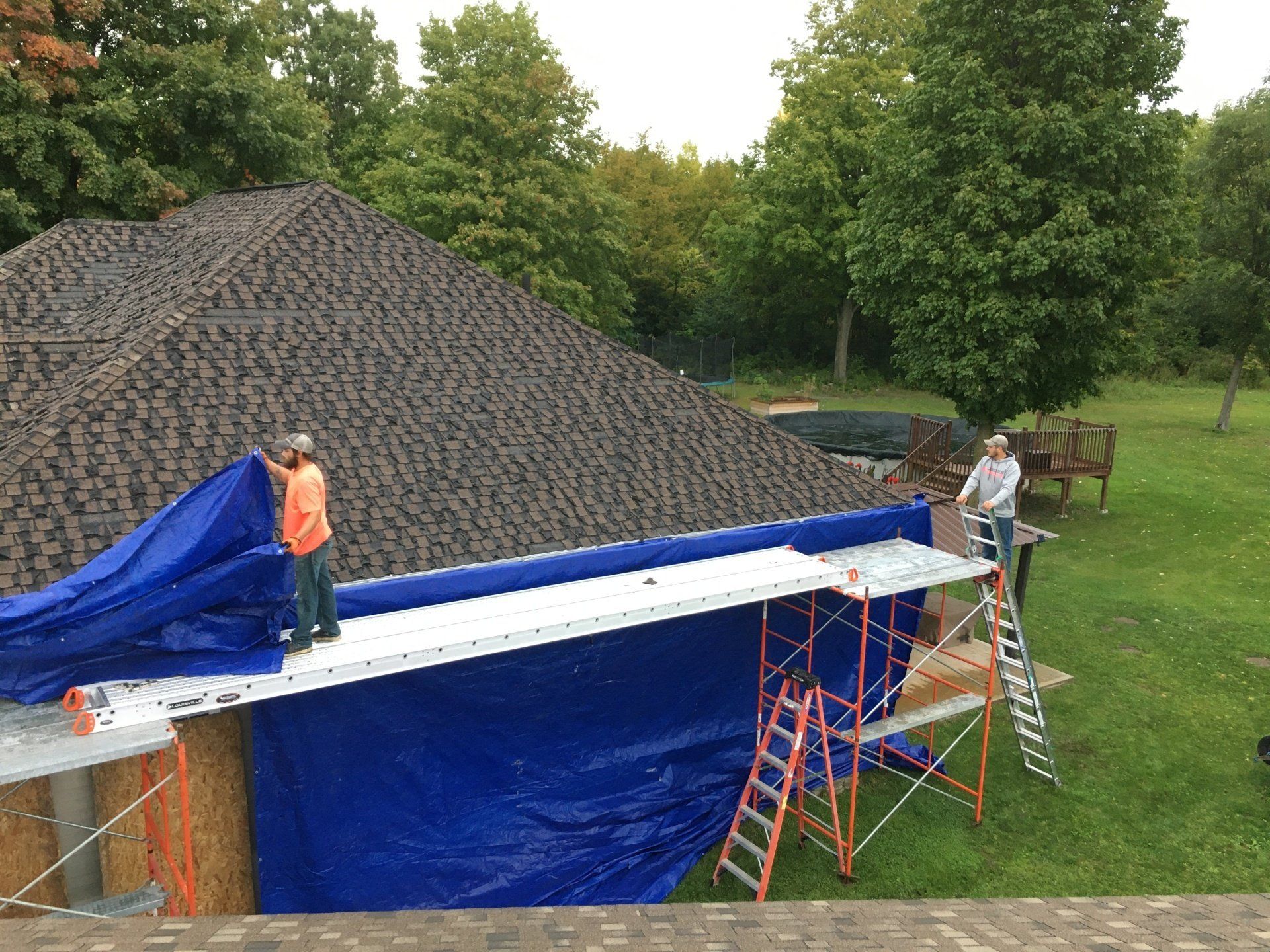 Two men are working on a roof with a blue tarp.