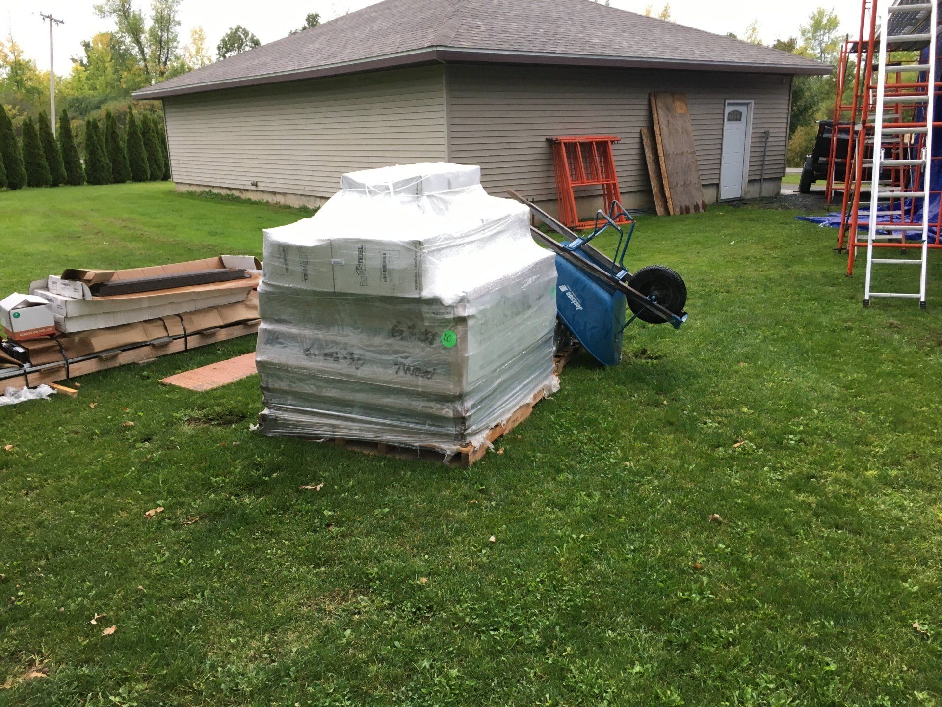 A wheelbarrow is sitting in the grass next to a stack of pallets.