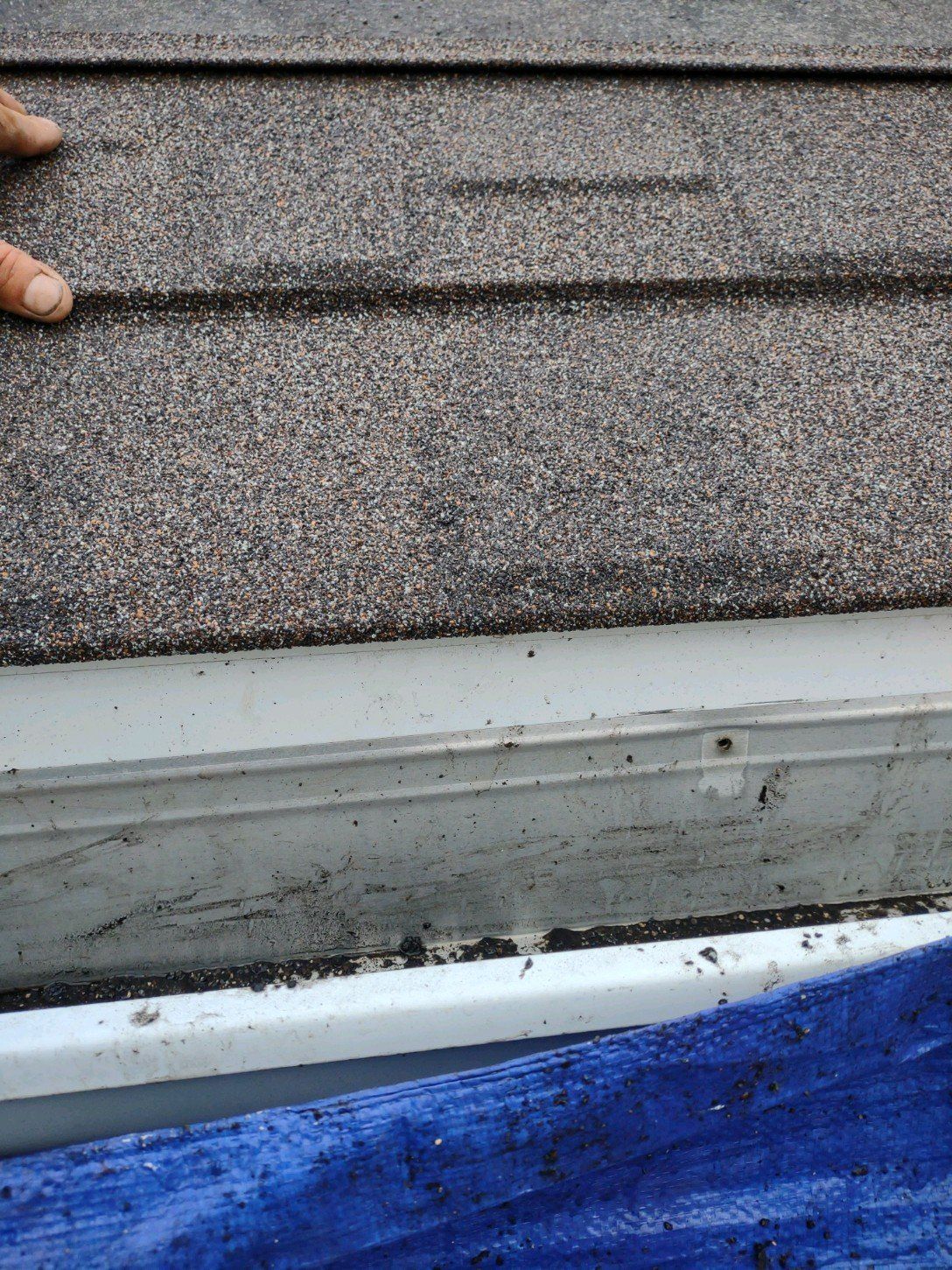 A person is standing on a roof next to a blue tarp.