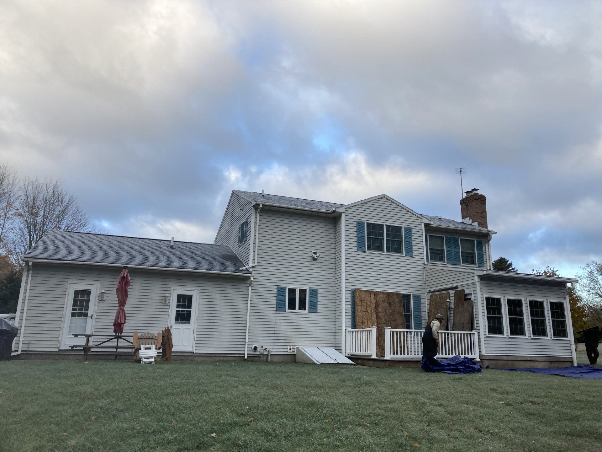 A large white house with a gray roof is sitting on top of a lush green field.