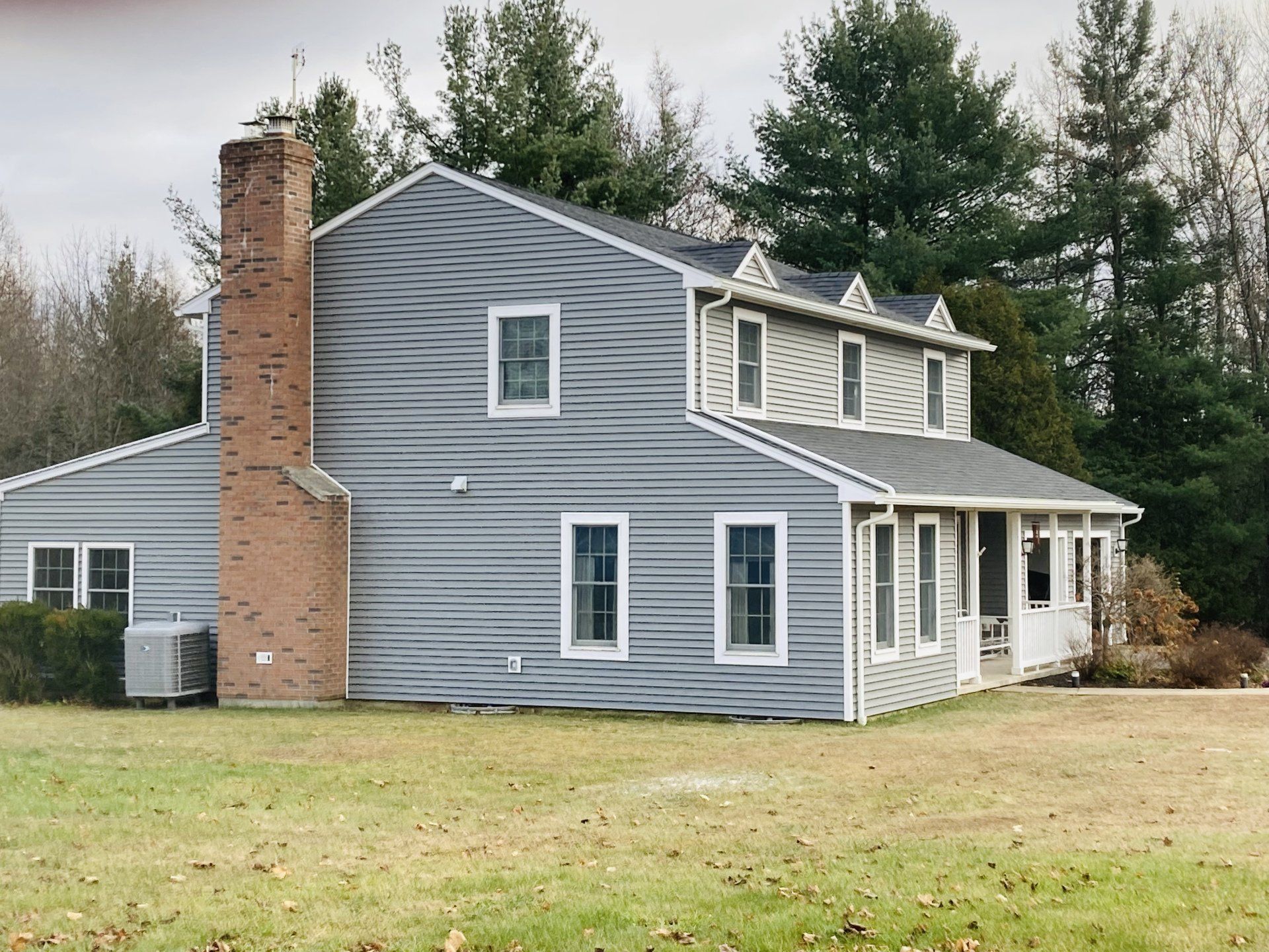 A large gray house with a brick chimney is surrounded by trees