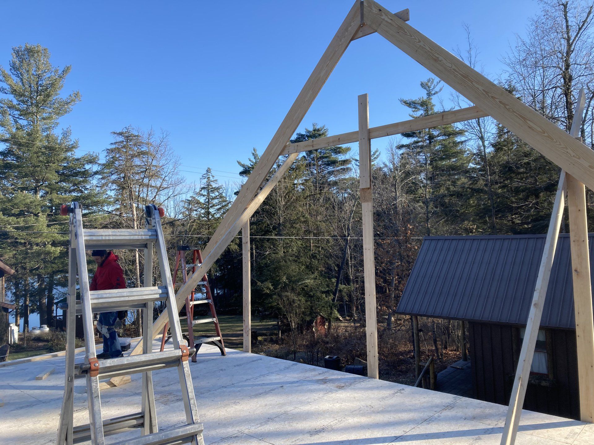 A man is sitting on a ladder in front of a wooden structure being built.