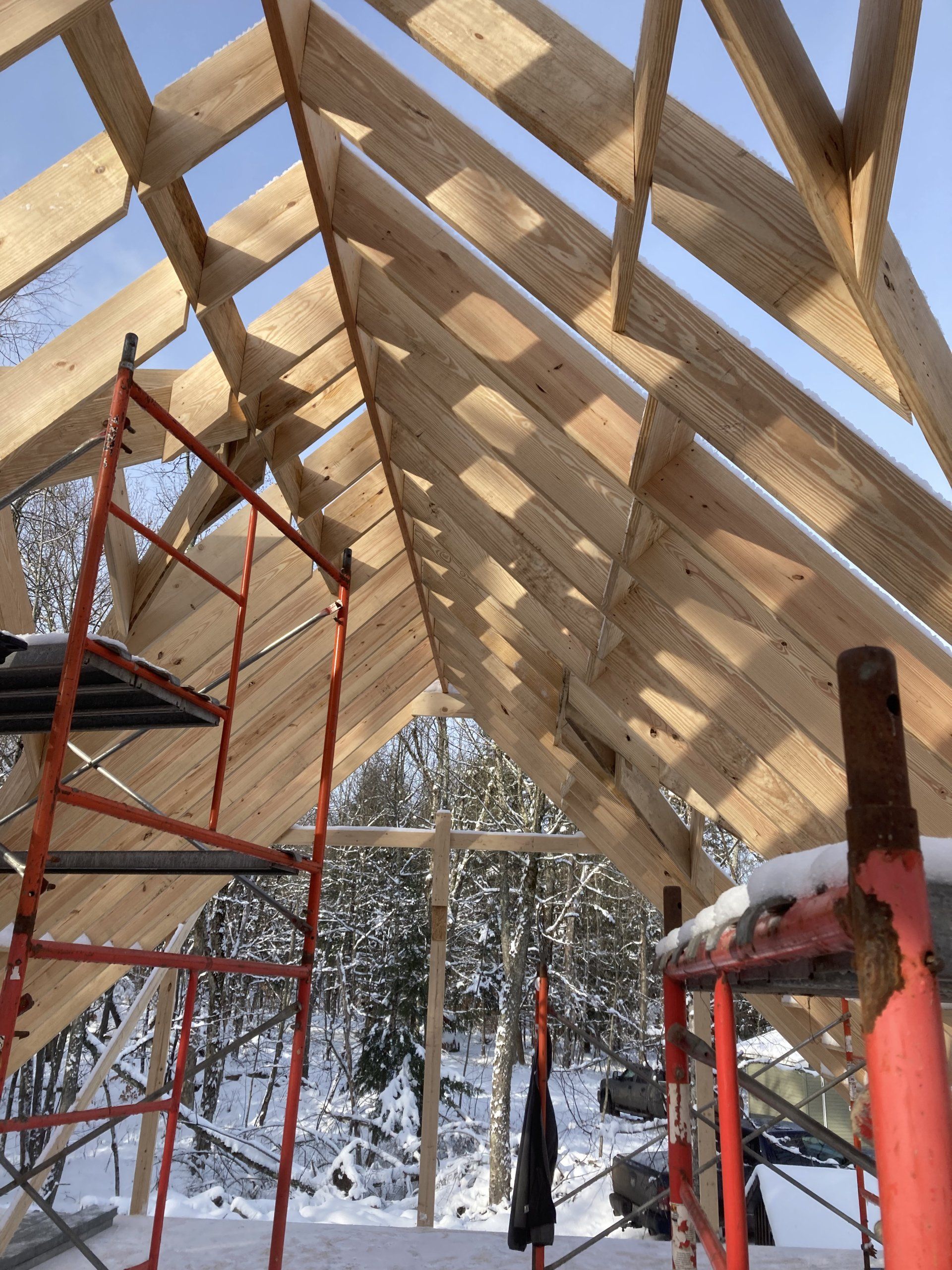 A wooden roof is being built in the snow with a ladder in the foreground.