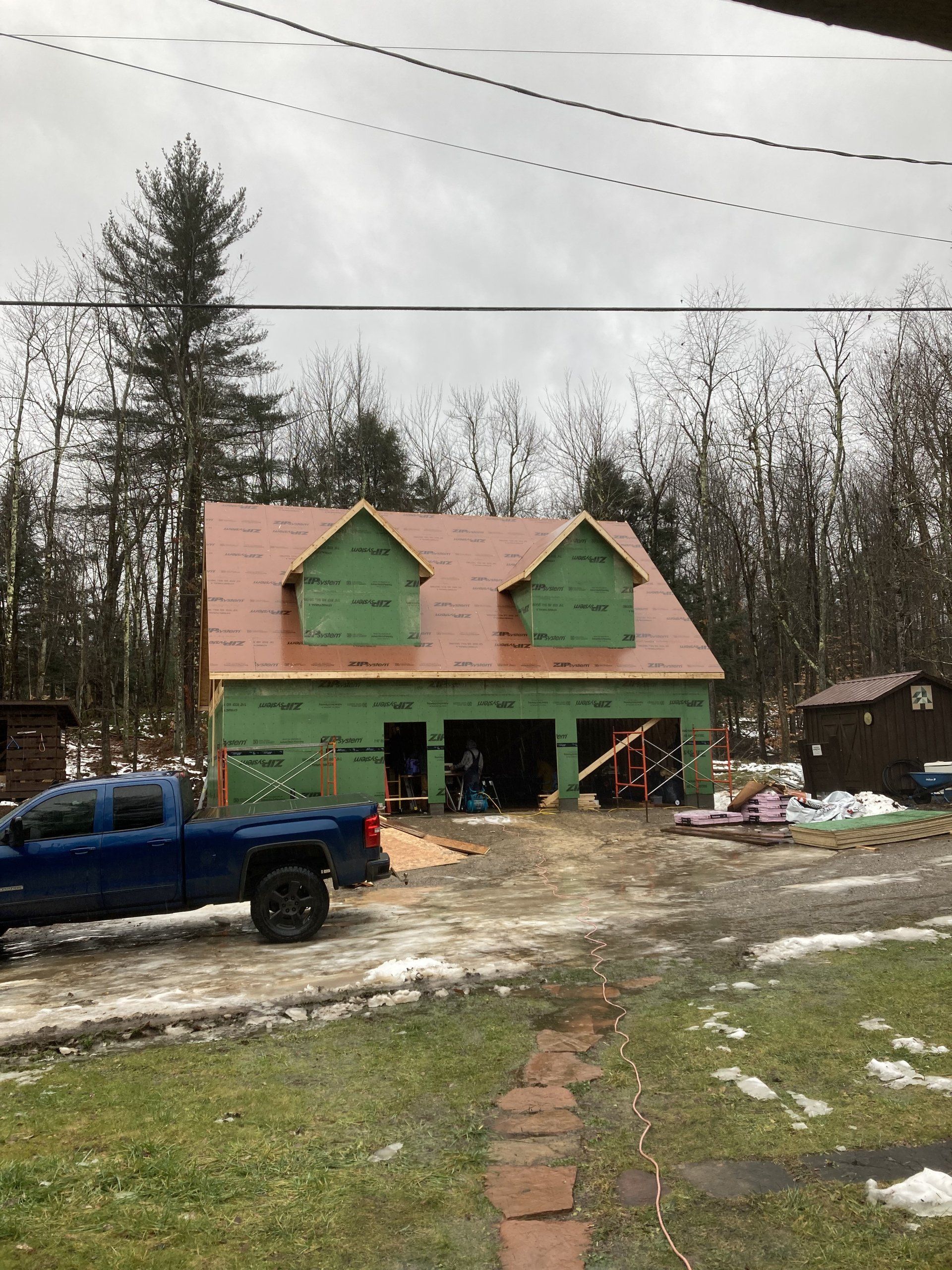 A blue truck is parked in front of a green house under construction