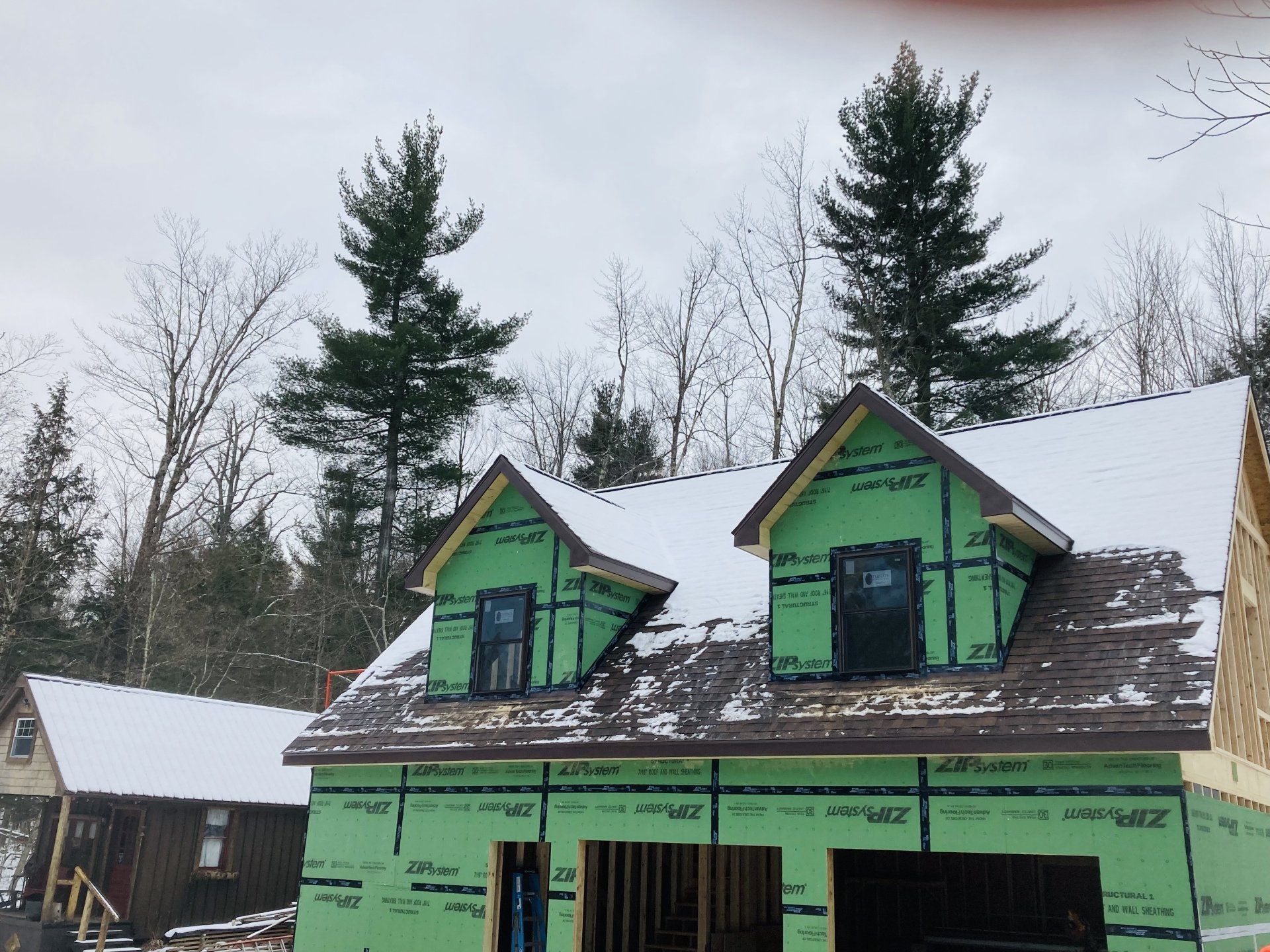 A house under construction with a green roof and trees in the background