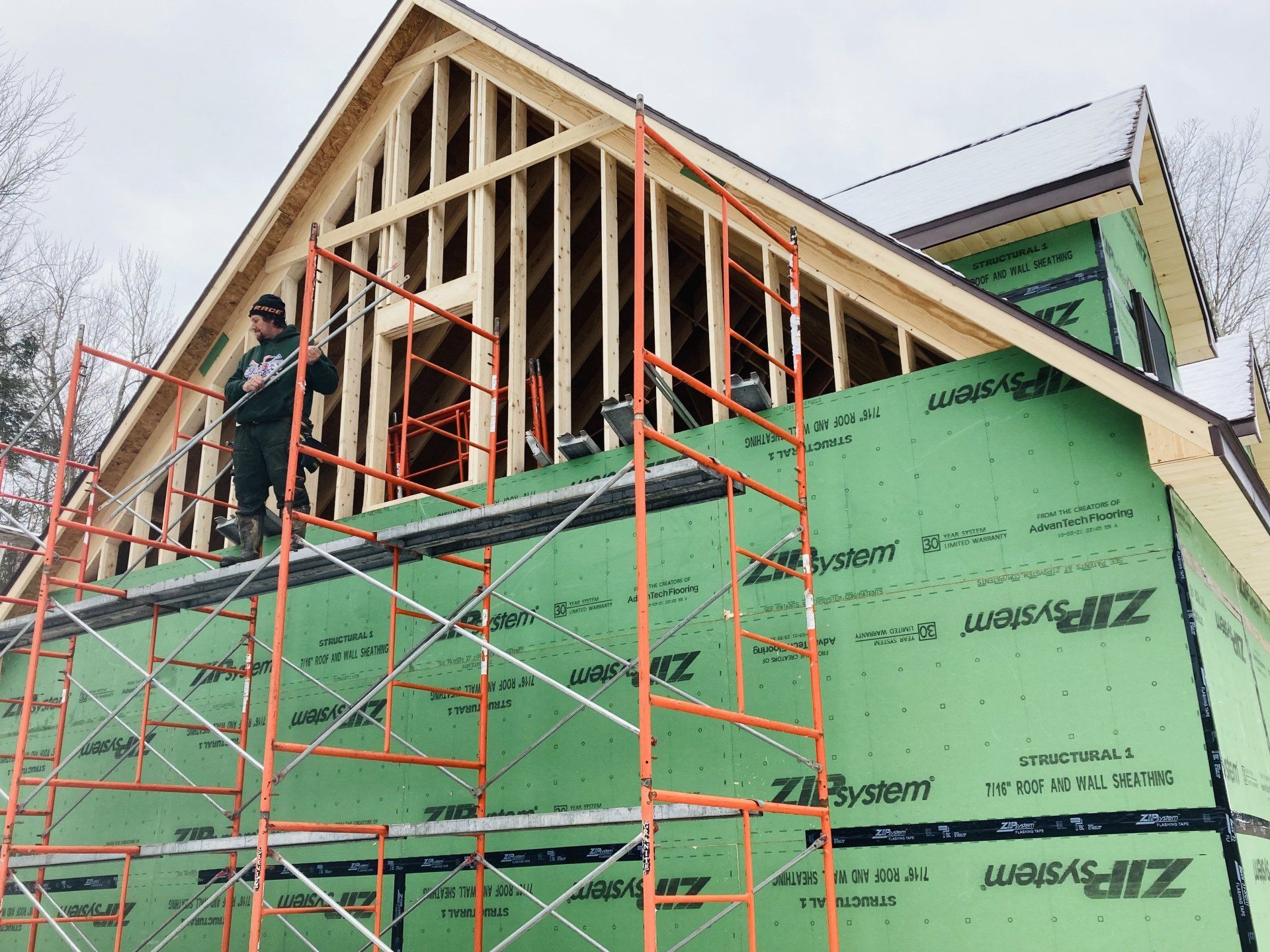 A man is standing on a scaffolding on the side of a house under construction.