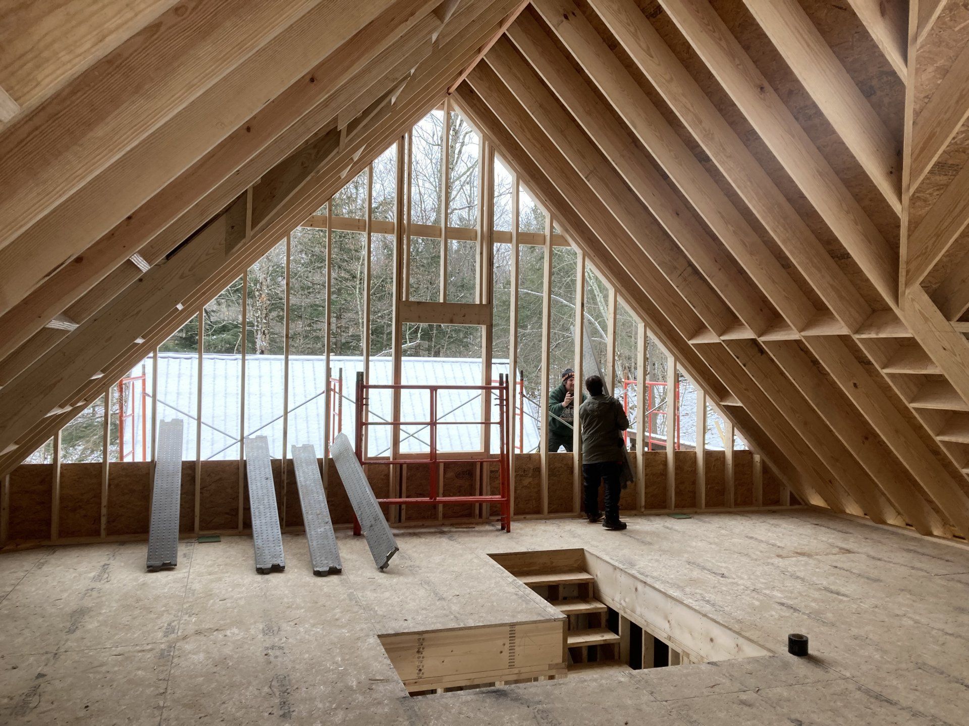 Two people are standing in the attic of a house under construction