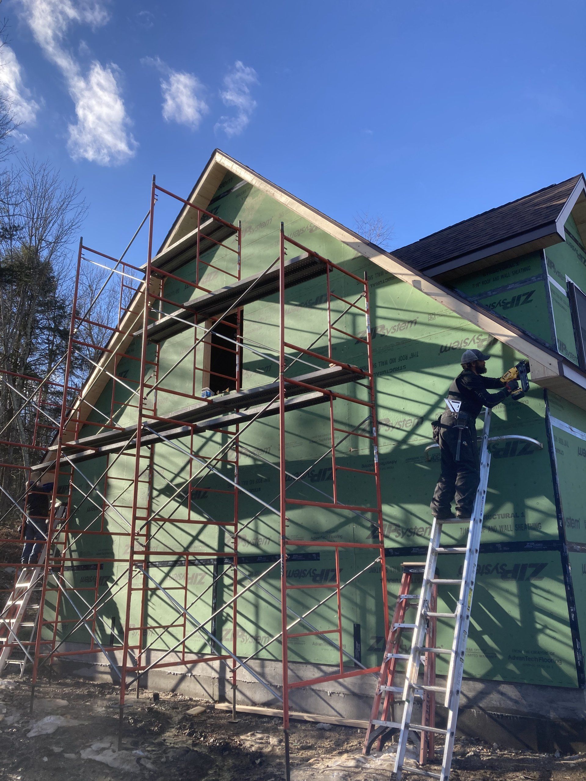 A man is standing on a ladder in front of a house under construction.